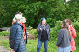 Mehrere Menschen zwischen 30 und 50 stehen auf einer Grünfläche, im Hintergrund sind Bäume. Die Menschen sind in einer regen, entspannte Diskussion. Sie tragen leichte Outdoor-Kleidung.